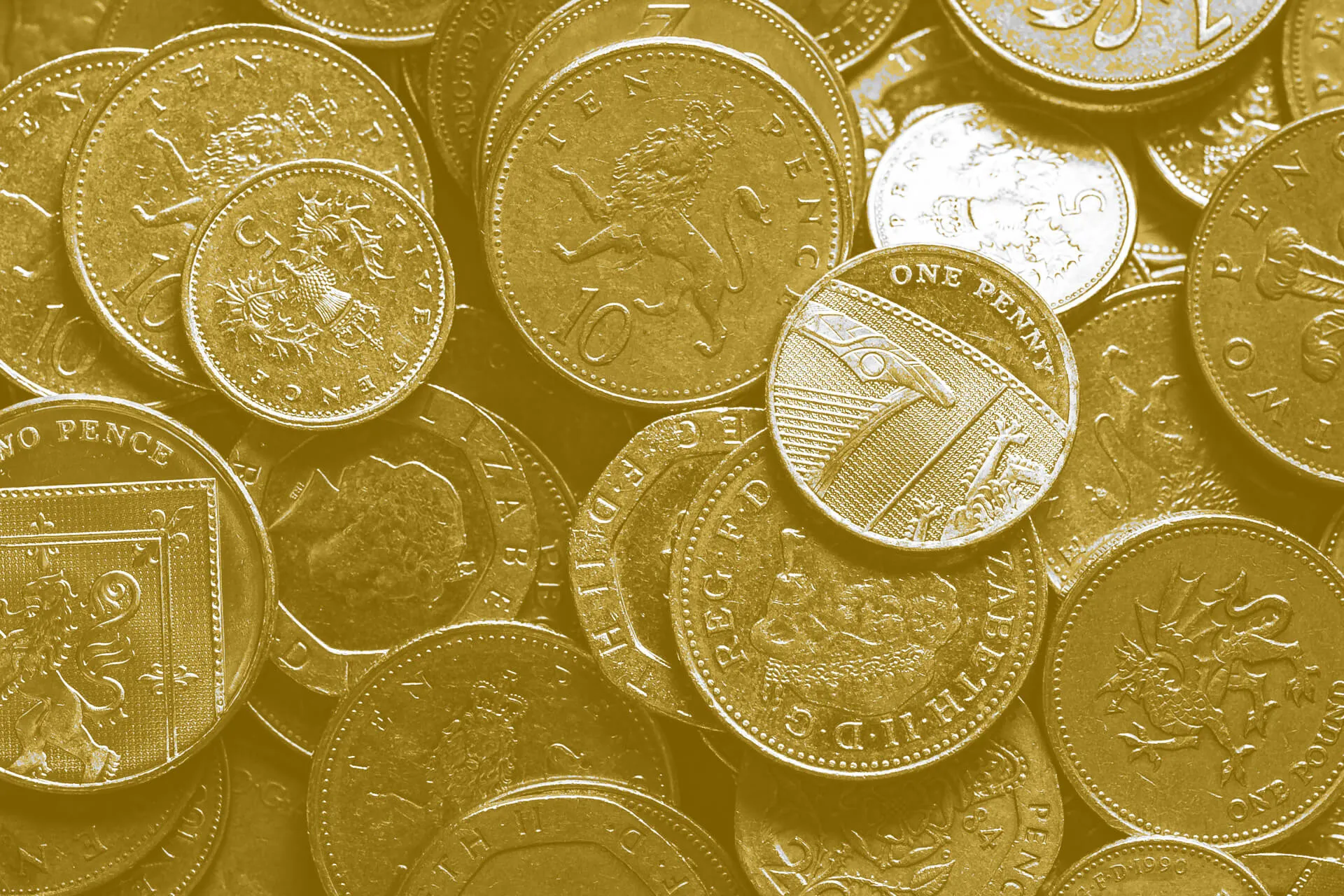 A close-up photograph of scattered British coins, including one pound and pence coins with golden colouring, showing various UK currency designs including the royal coat of arms and shield emblems.